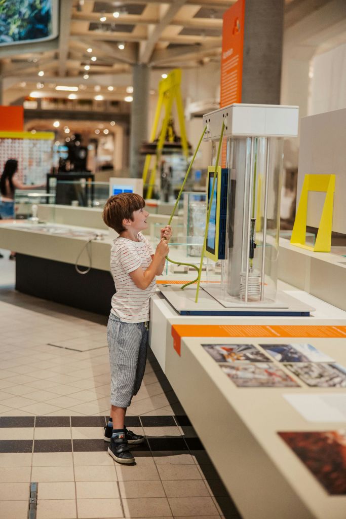 한 어린이가 과학 박물관의 전시물과 상호 작용하며 높은 원통형 디스플레이 옆에 레버를 당깁니다.