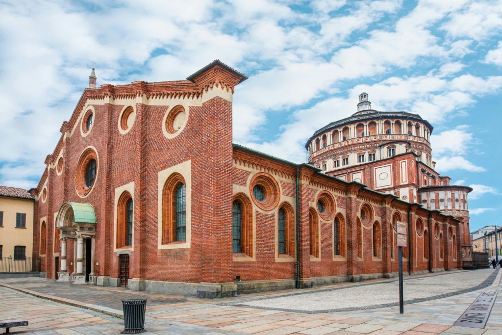 둥글고 화려한 구조에 인접한 아치형 창문과 원형 디자인의 붉은 벽돌 건물. 머리 위로 구름이 낀 푸른 하늘.