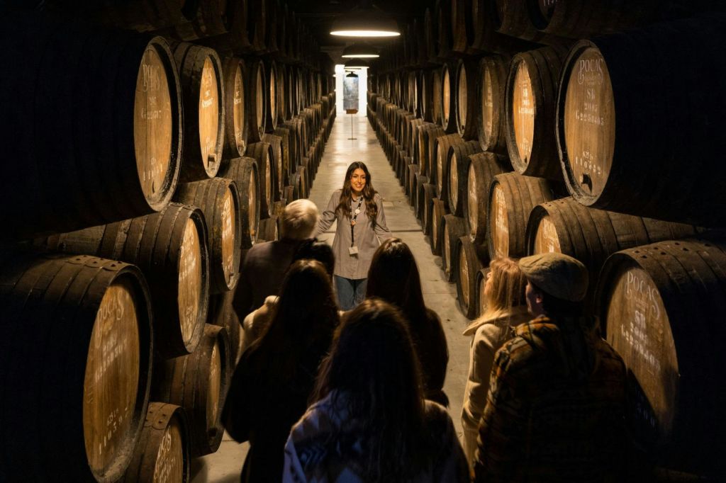 양쪽 벽을 따라 나무 통이 늘어선 조명이 희미한 방에서 일행과 이야기를 나누는 투어 가이드.