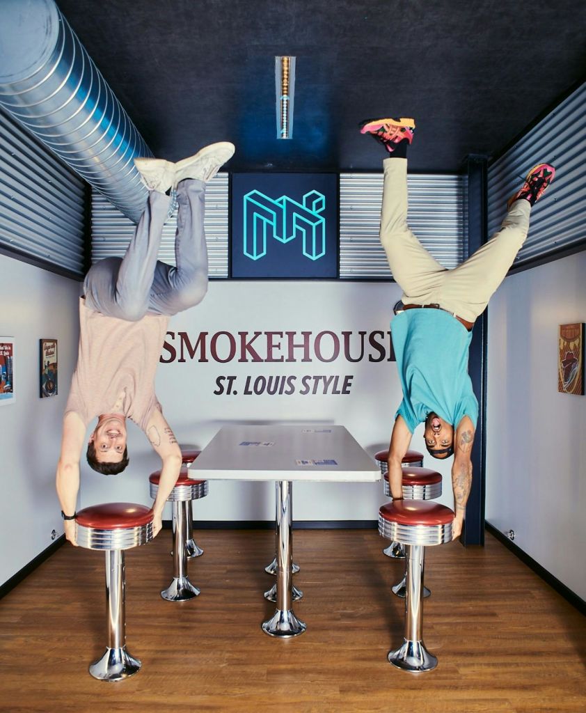 'Smokehouse St. Louis Style' 간판을 배경으로 복고풍 스타일의 다이너에서 두 사람이 거꾸로 포즈를 취하고 있습니다.