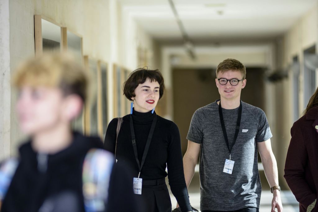 랜야드를 착용한 세 명이 복도를 걸어가고, 두 명은 초점이 맞지 않고 미소를 짓고, 한 명은 초점이 약간 어긋납니다.