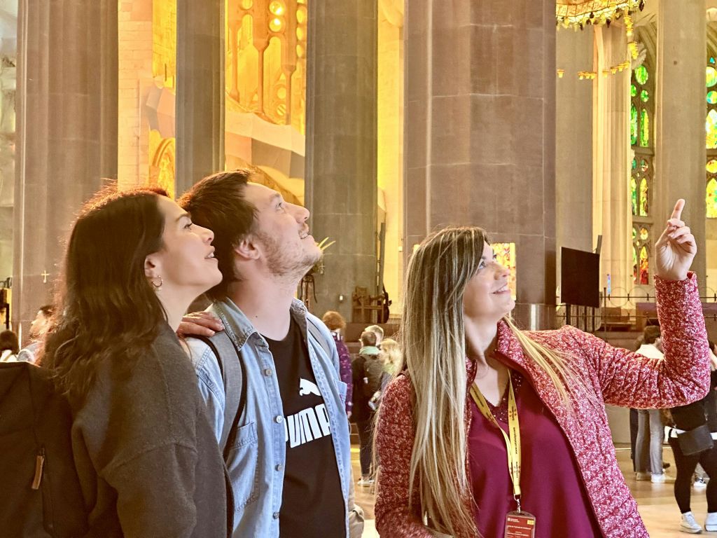 세 사람은 높은 기둥과 화려한 황금 장식이 있는 웅장한 건물 내부에서 경외심을 느끼며 위를 바라봅니다.