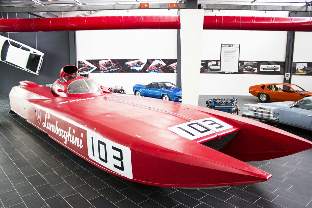 빈티지 자동차가 전시된 쇼룸에 "103" 이라고 표시된 레드 람보르기니 스피드보트가 있고, 배경에는 스탠드가 있습니다.