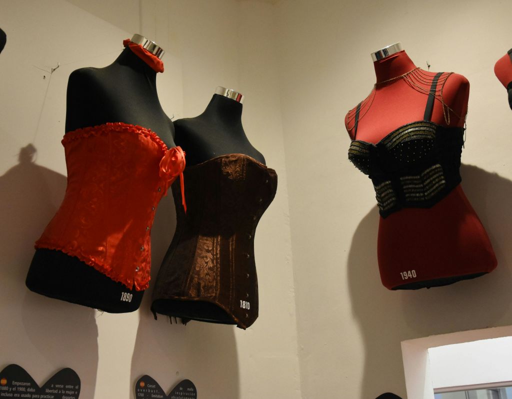 1980년산 빨간색, 1890년산 갈색, 1940년산 검정색과 빨간색 등 세 개의 마네킹이 빈티지 코르셋을 전시하고 있습니다.