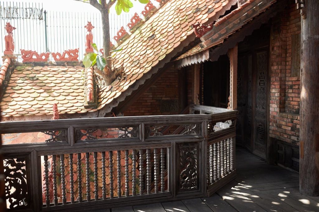 정교한 조각이 있는 전통적인 목조 발코니에서는 비스듬한 타일 지붕과 푸른 잎이 있는 나무가 내려다보입니다.
