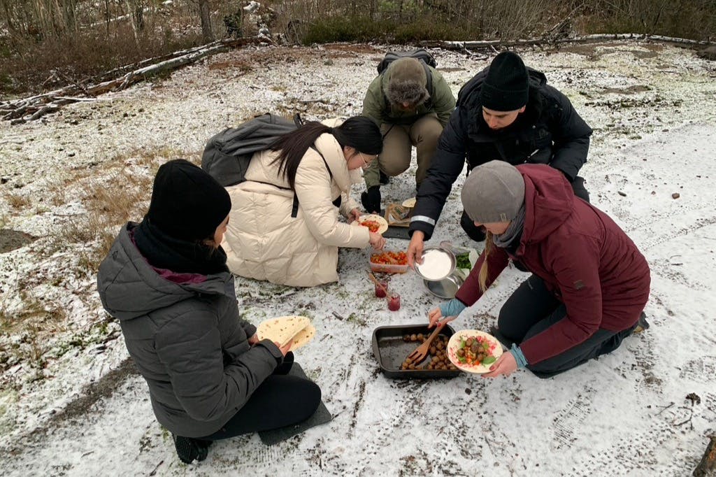 4명의 사람이 눈 덮인 땅에서 야외에서 트레이에서 음식을 준비하고 나누고 있으며, 한 명은 랩을 들고 있습니다.