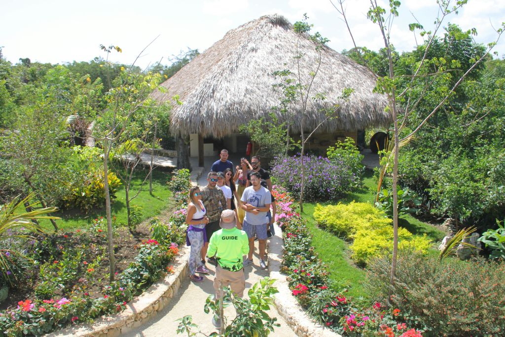 투어 가이드가 한 무리의 사람들을 이끌고 다채로운 꽃들이 늘어선 정원길에서 초가지붕 오두막으로 안내합니다.
