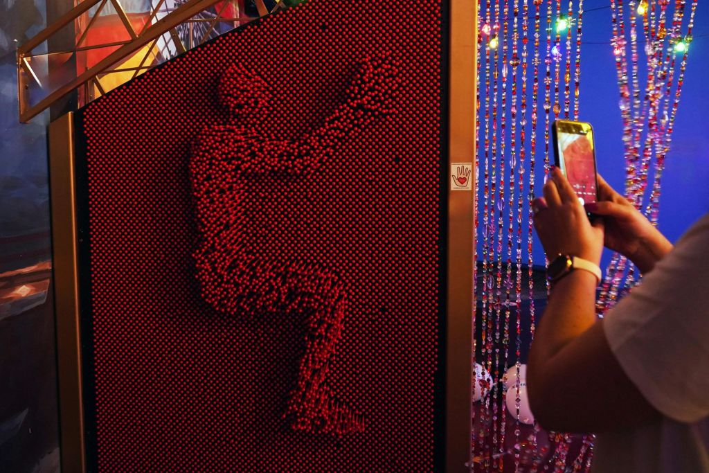 앉아있는 포즈를 취하고 근처에 사진을 찍는 사람의 모습이 그려진 빨간색 핀 아트 보드.