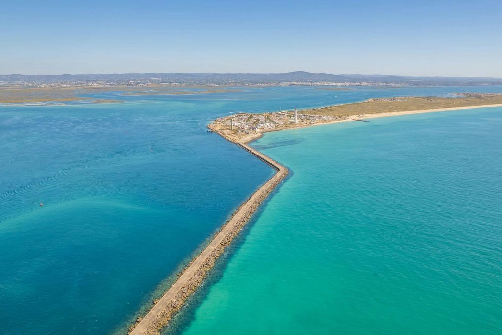 청록색과 깊고 푸른 바다로 둘러싸인 등대가 있는 해안 마을로 이어지는 긴 부두의 공중 전망.