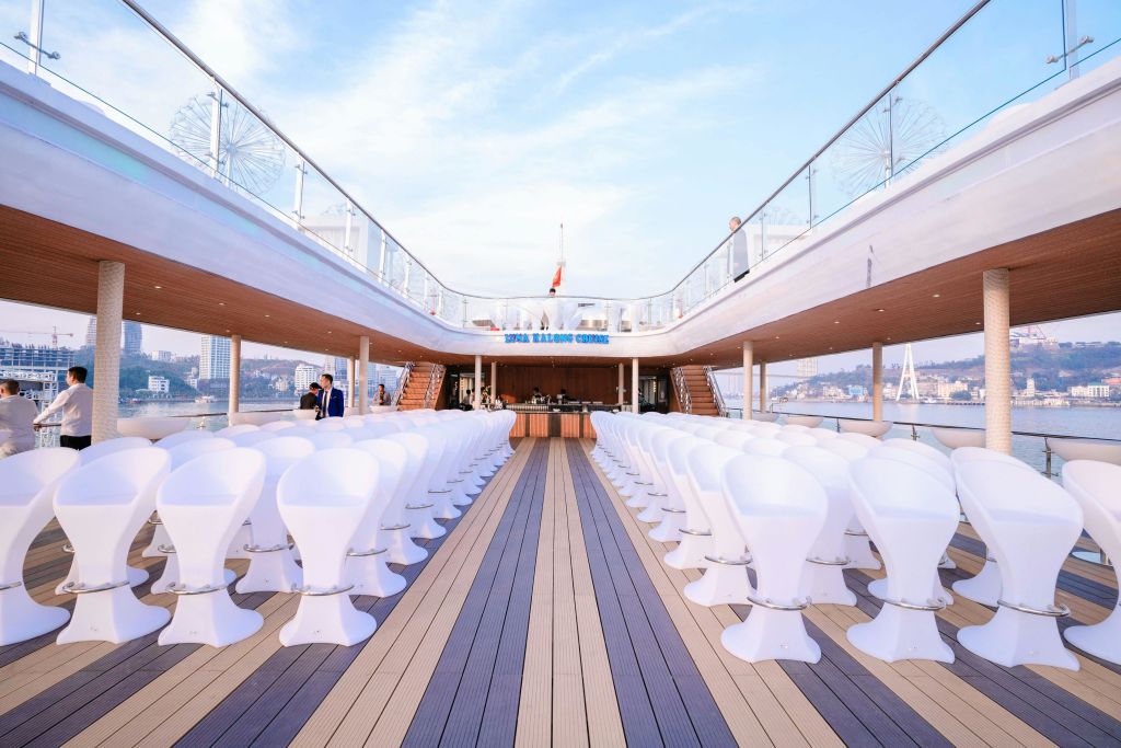 무대와 마주한 흰색 의자가 줄지어 있는 배의 갑판. '왕실 풍선' 표지판이 보이고 맑은 하늘을 배경으로 도시의 스카이라인이 펼쳐집니다.