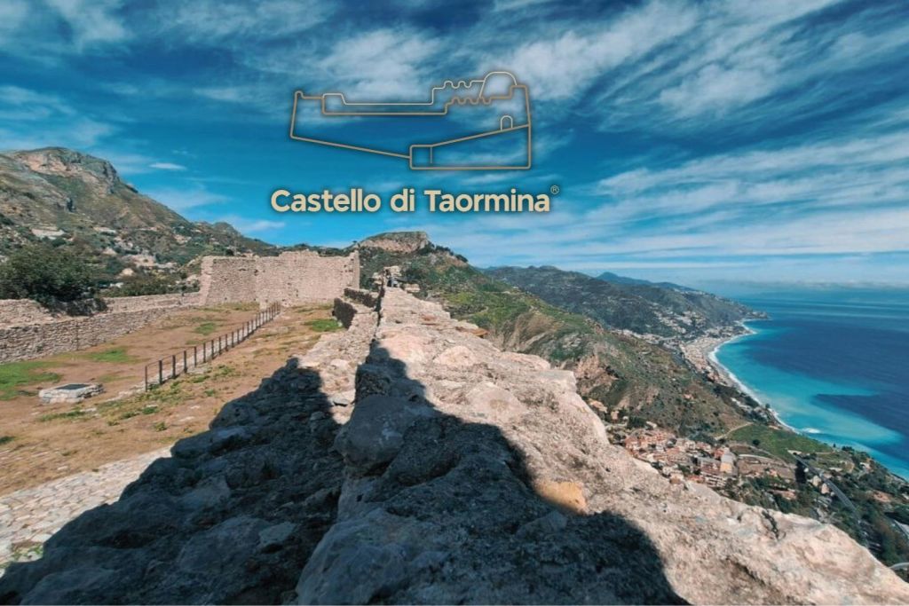 해안 풍경, 푸른 하늘, 전경의 돌길에 그림자가 있는 카스텔로 디 타오르미나 유적의 전망.