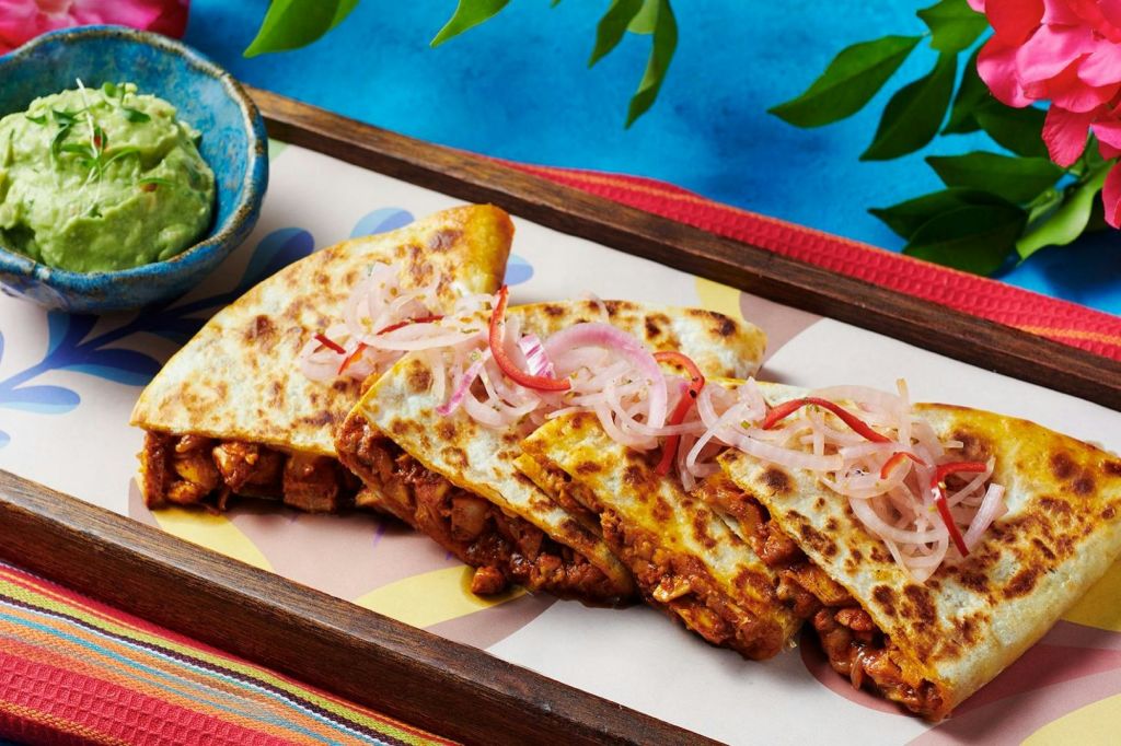 양념된 고기를 채우고 쟁반에 절인 붉은 양파를 얹은 세 개의 퀘사디야 웨지. 과카몰리는 근처의 파란색 그릇에 담겨 있습니다.