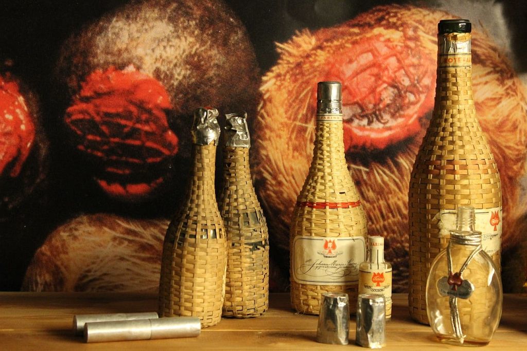 레이블이 있는 큰 병 1개와 질감이 살아있는 배경으로 나무 표면에 놓인 미니어처 병을 포함하여 4개의 고리버들 포장된 병.