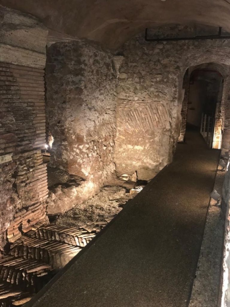 돌담과 벽돌로 된 아치가 있는 고대 지하 복도는 어두운 조명으로 아치형 통로로 이어집니다.