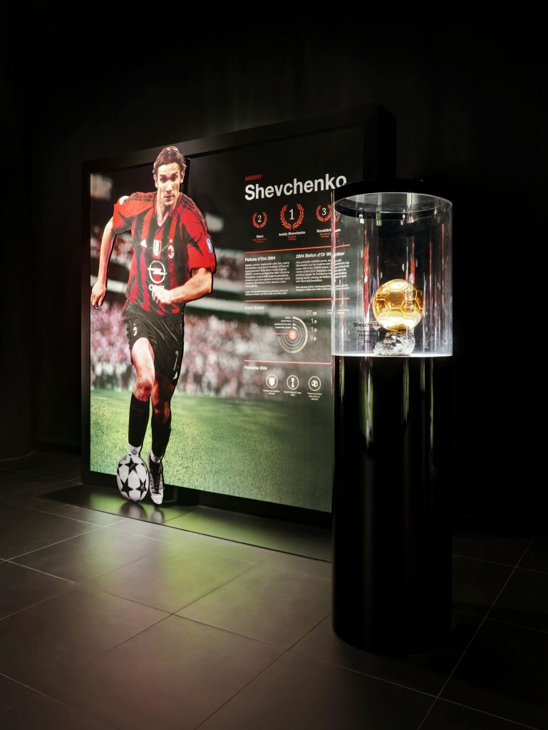 포스터 배경과 유리로 둘러싸인 황금 공 트로피가 있는 셰브첸코라는 이름의 축구 선수가 전시되어 있습니다.