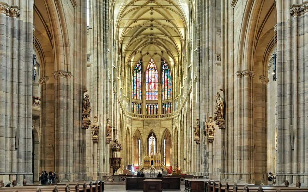 아치형 천장, 조각상, 목조 동굴, 전면에 커다란 스테인드글라스 창문이 있는 대성당의 내부.