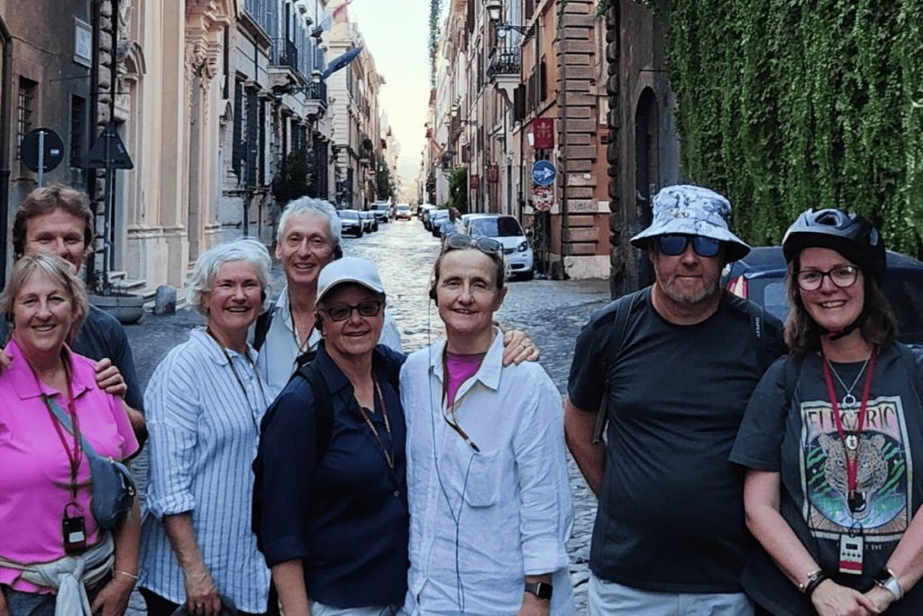 주차된 자동차와 유서 깊은 건물이 늘어선 자갈길에서 다섯 명이 포즈를 취하고 있습니다.