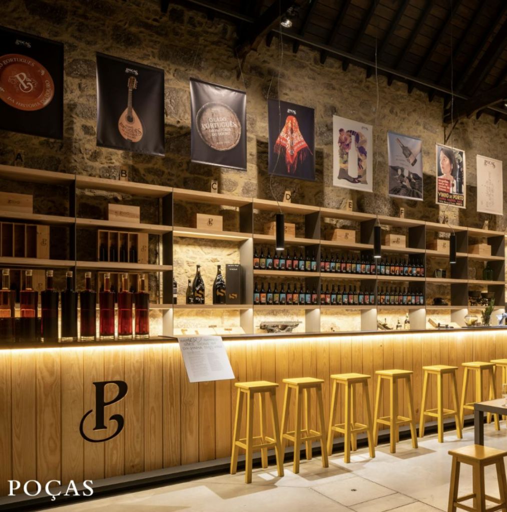 나무 스툴, 카운터, 선반이 있는 세련된 바 공간으로, 벽에 와인병과 장식품이 구비되어 있습니다.