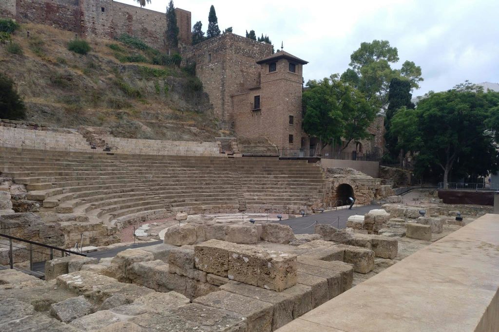 나무를 배경으로 오래된 건물에 인접한 고대 석조 원형극장 계단과 유적.