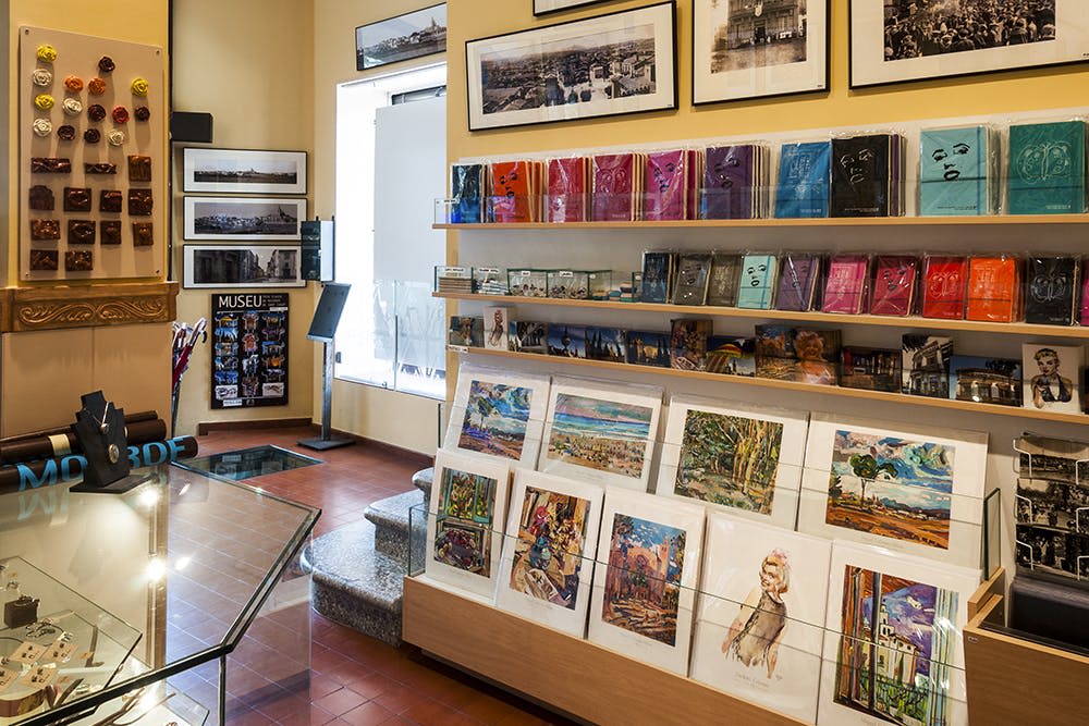 벽에 액자에 담긴 예술품, 책, 엽서, 아트 프린트가 진열된 선반이 있는 박물관 선물 가게입니다.