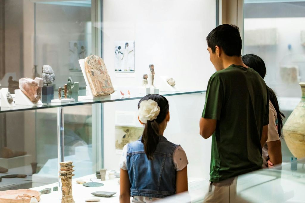 뒤에서 본 세 사람은 박물관의 유리 진열장에서 고대 유물을 관찰합니다.