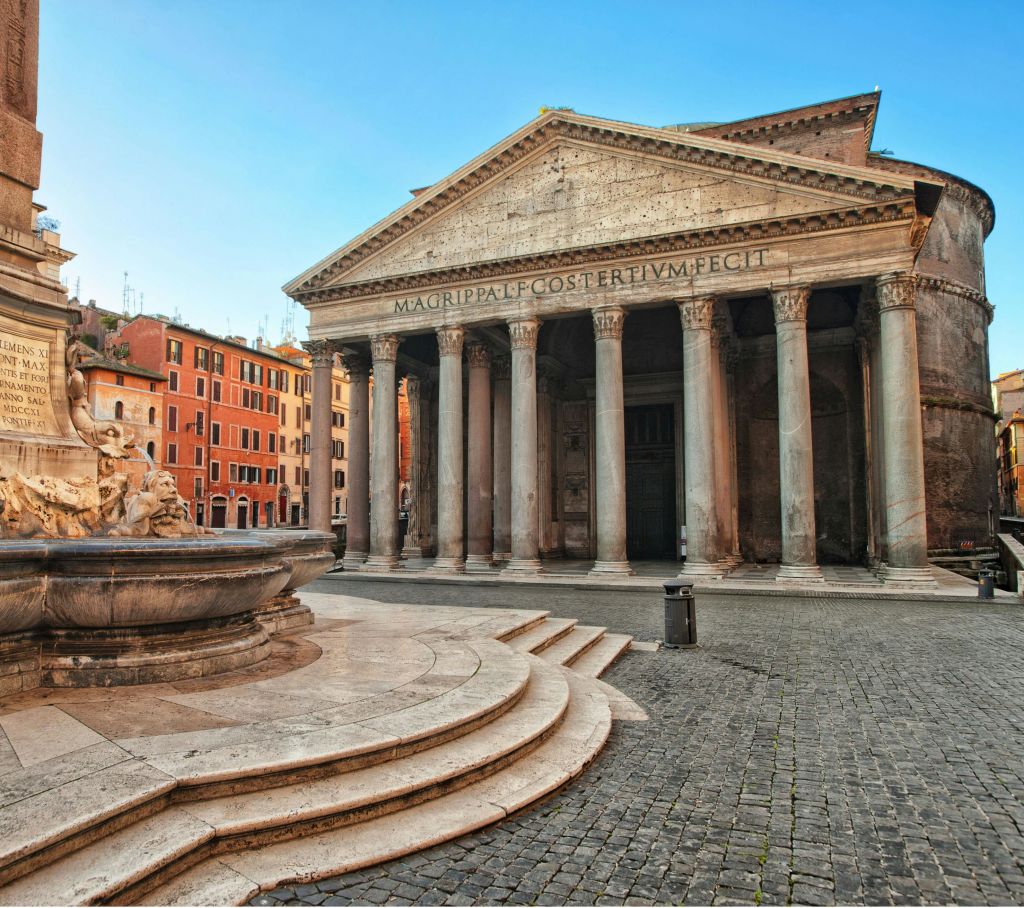 자갈 광장의 분수에 인접한 외관에 높은 기둥과 라틴 문양이 있는 역사적인 건물입니다.