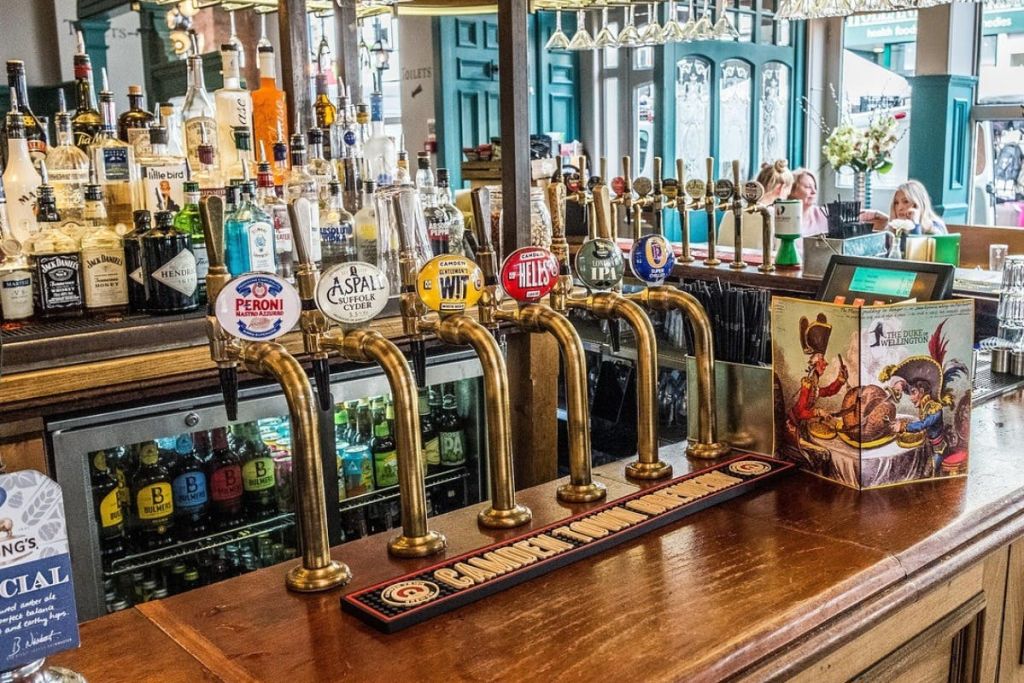 술집 내부에는 황동 맥주 탭이 있는 바 카운터가 있으며, 각각 다른 브랜드로 표시되어 있으며, 병을 배경으로 선반이 있습니다.