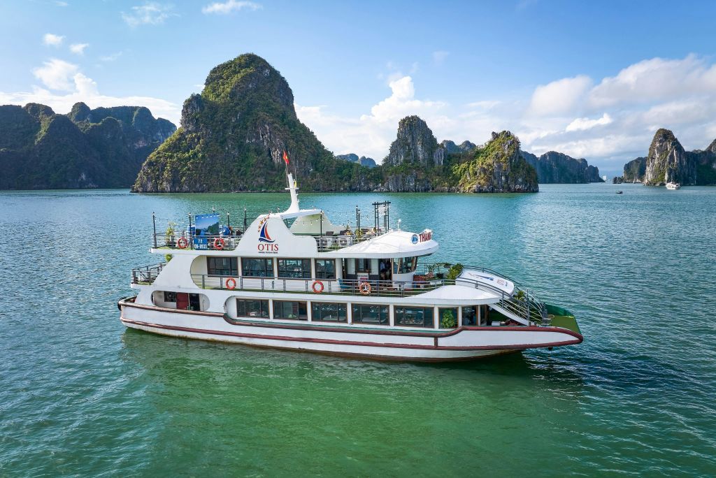 "오티스" 라는 이름의 흰색 페리 보트가 청명한 하늘 아래 석회암 섬을 배경으로 잔잔한 청록색 바다를 항해합니다.