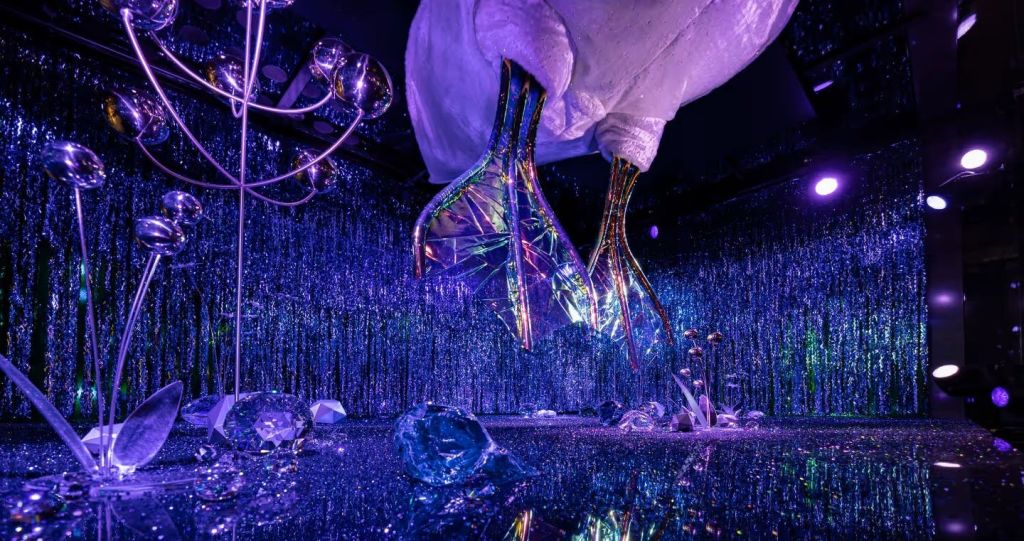 반짝이는 보라색 조명, 반사 표면, 추상적인 조형물이 천상의 분위기를 연출하는 초현실적인 객실입니다.