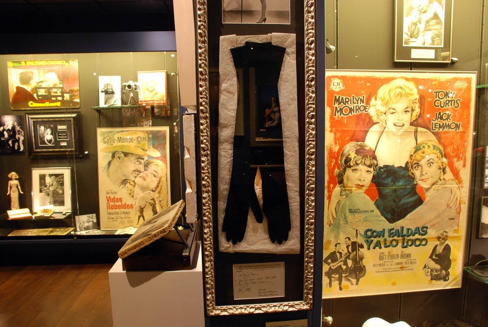 마릴린 먼로, 토니 커티스, 잭 레먼이 등장하는 빈티지 "Some Like It Hot" 영화 포스터 옆에 검은색 장갑이 액자에 담겨 있습니다.