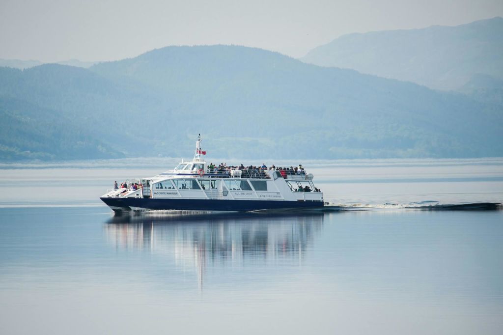 산을 배경으로 잔잔한 호수에서 승객을 태우고 항해하는 페리입니다.