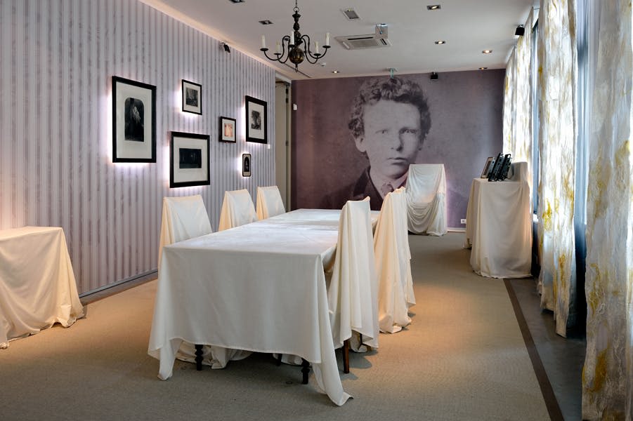 흰색 천으로 덮인 테이블과 의자, 벽에 커다란 빈티지 초상화, 액자 사진, 샹들리에, 커튼이 있는 객실입니다.