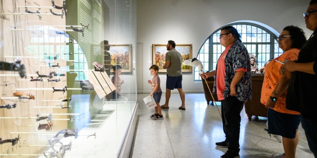 예술품과 커다란 아치형 창문을 배경으로 취미용 말을 들고 있는 사람들이 미술관에 서 있습니다.