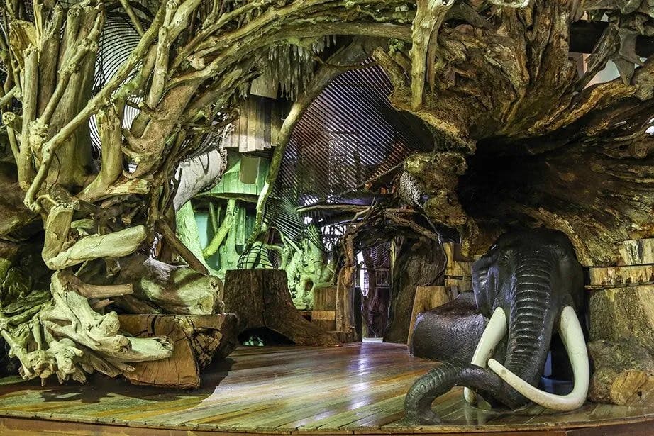 정교한 목재와 뿌리 구조를 갖춘 실내 공간으로 커다란 코끼리 조각과 다양한 예술적 요소가 특징입니다.