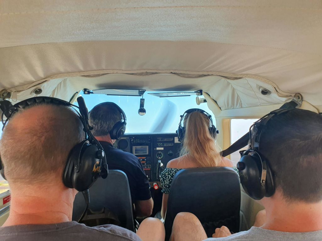 작은 비행기 조종석에 앉아 헤드셋을 착용하고 있는 4명의 사람들로, 조종 장치와 창문이 보입니다.