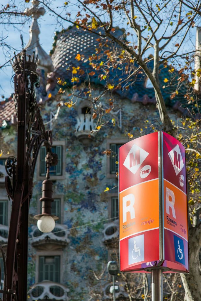 나무와 장식 가로등이 있는 화려하고 장식적인 건물 앞에 있는 지하철과 렌페 기차역을 나타내는 표지판.