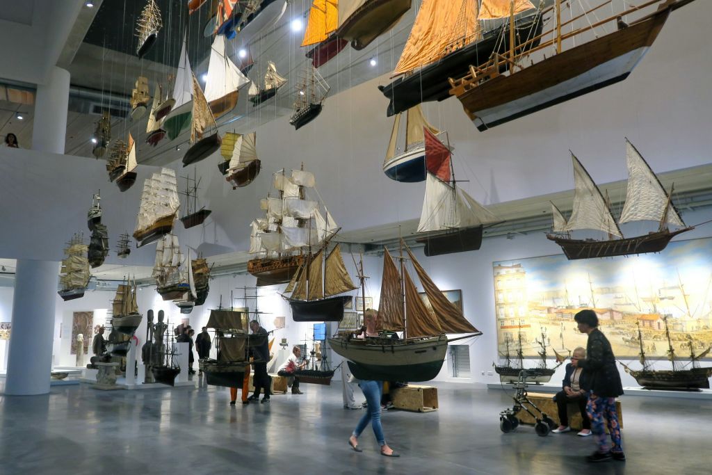 수많은 모형 선박을 전시하는 박물관 전시관에는 방문객들이 걷고 세부 복제품을 관찰합니다.