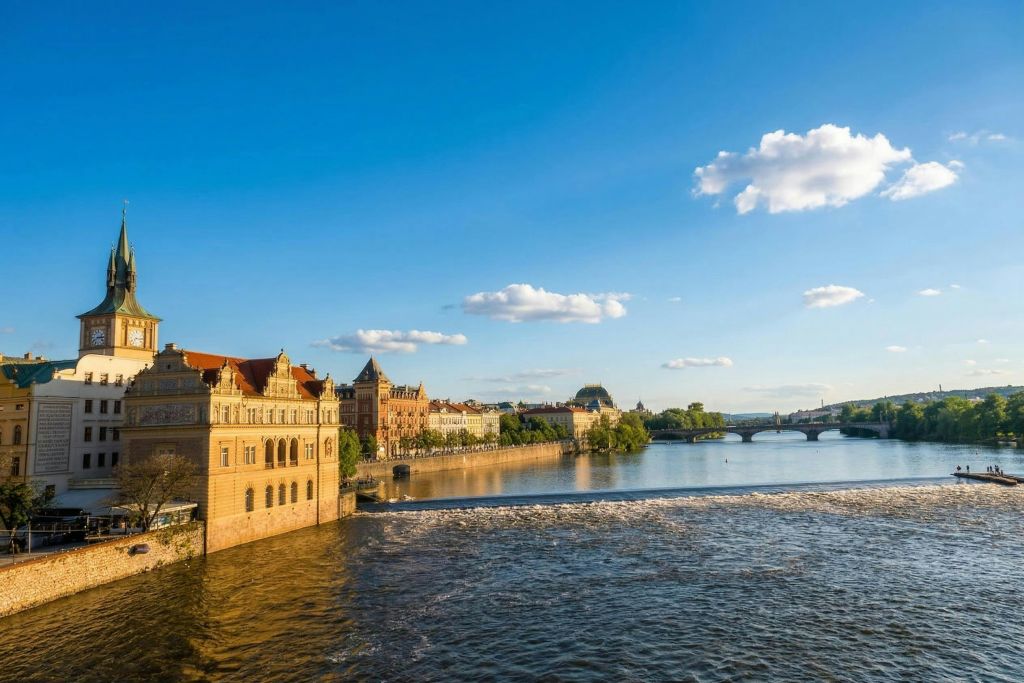 역사적인 건물, 다리, 구름이 흩날리는 푸른 하늘 아래 잔잔한 강이 흐르는 강변 도시의 경치.