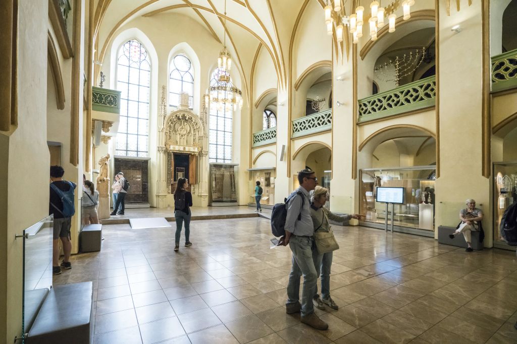 사람들은 아치형 창문, 샹들리에, 역사적 유물이 전시된 넓고 조명이 밝은 박물관 홀을 탐험합니다.