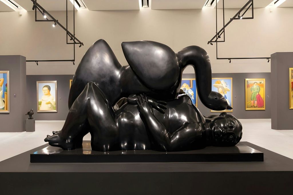 벽에 액자 그림이 그려진 현대 미술관의 추상적이고 기대어 있는 대형 검은색 조각상입니다.