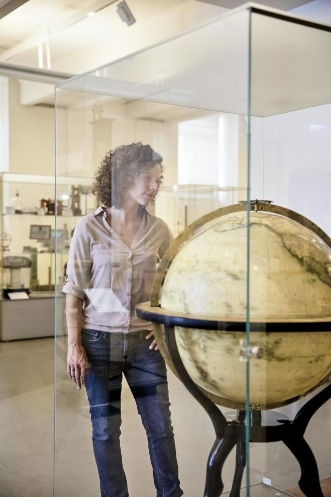 곱슬머리를 한 사람이 조명이 밝은 현대적인 박물관 전시관에서 유리로 둘러싸인 커다란 지구본을 살펴봅니다.