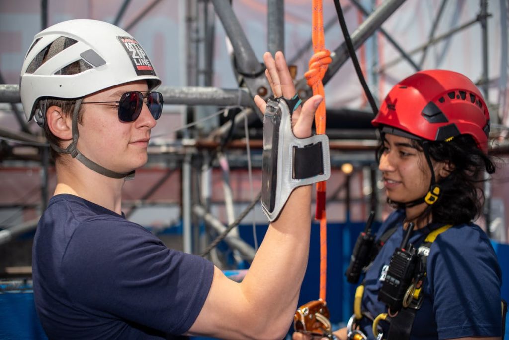헬멧과 안전 장비를 착용한 두 사람이 비계 구조물에서 등반 장비와 상호 작용합니다.