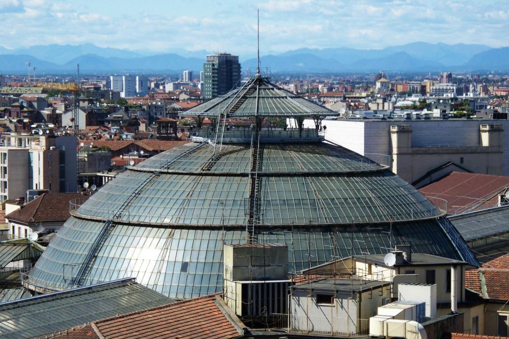 도시 경관에 금속 프레임워크가 보이는 대형 유리 돔형 건물. 고층 건물과 산을 배경으로.