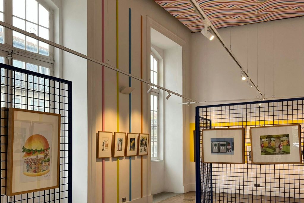 줄무늬 벽에 액자 그림, 커다란 창문, 천장 조명, 줄무늬 천장이 있는 미술관입니다.