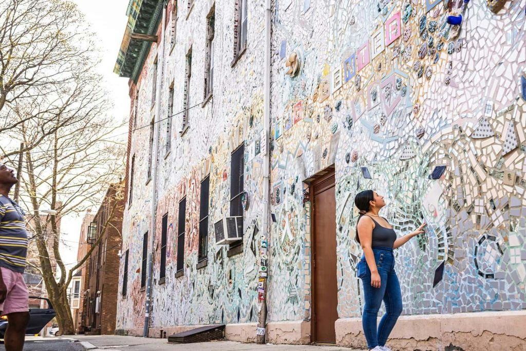 화창한 날에 한 여성이 서서 화려한 모자이크 작품으로 뒤덮인 건물을 감상하고 있습니다.
