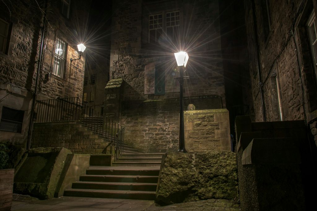 계단, 가로등, 유서 깊은 벽돌 건물이 있는 어두운 밤의 석조 골목길.