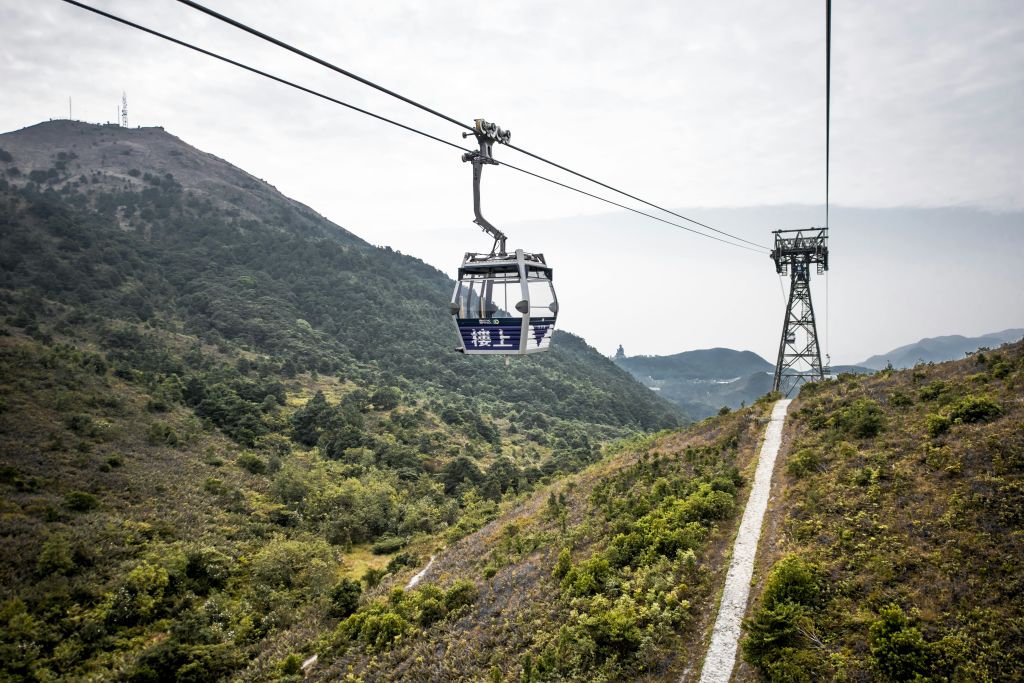안개 낀 하늘을 배경으로 울창하고 산이 많은 풍경 위로 케이블카가 지나갑니다.