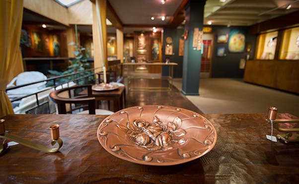 다양한 예술 작품을 배경으로 미술관의 목재 표면에 꽃무늬 디자인이 진열된 장식용 접시입니다.