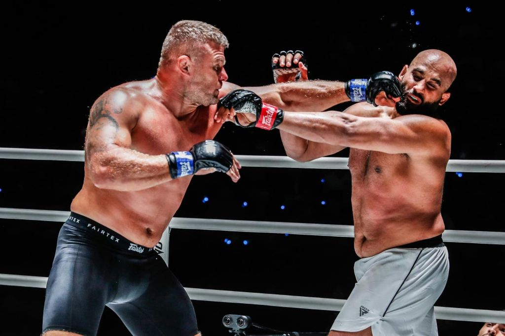 셔츠가 없는 두 명의 남성 MMA 전투원이 장갑과 반바지를 착용한 채 링에서 펀치를 교환합니다.