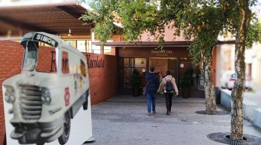 왼쪽에 주차된 차량이 있고 머리 위로 나무가 있는 사이먼 콜 초콜릿 가게 입구를 향해 걸어가는 두 사람.